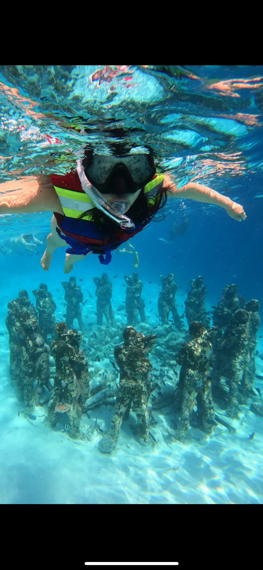 Snorkeler above the underwater statues covered in marine life