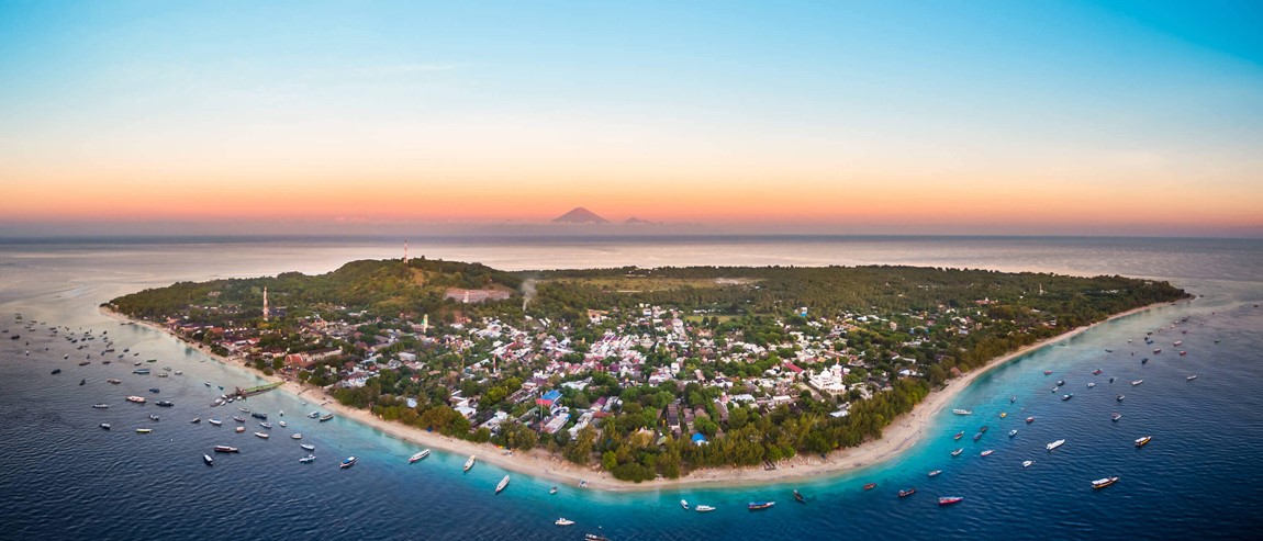 Aerial view of Gili Trawangan island at sunset with Mount Bali volcano in the distance